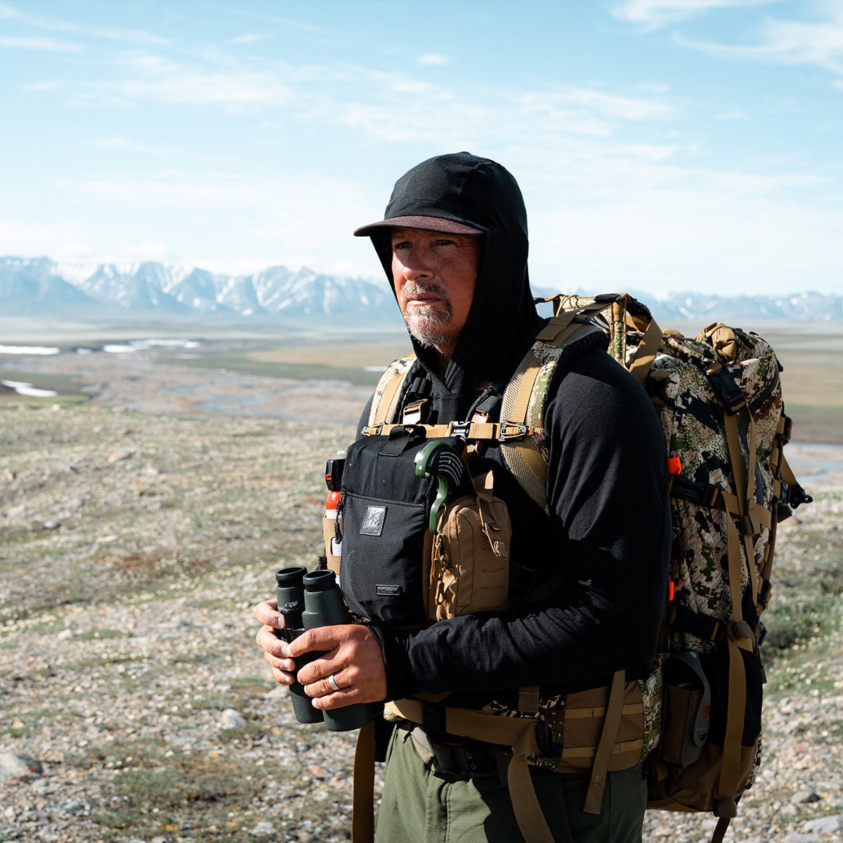 Casey Anderson carrying his field pack and binoculars in the mountains